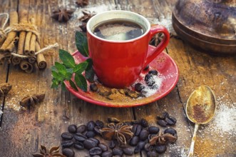 Red glass Cup with coffee on wooden background strewn with aromatic spices to drink