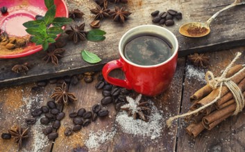 Red glass Cup with coffee on wooden background strewn with aromatic spices to drink