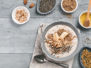 Overnight oats in bowl and ingredients - banana, LSA, chia seeds, almond, honey and pollen on gray