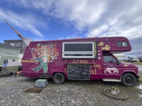 Food truck with colourful wall art and a menu in front of a cloudy street, Homer, Alaska, USA,