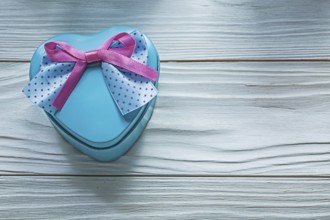 Heart-shaped blue gift box with pink bow on wooden board holidays concept