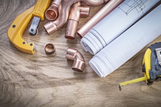 Construction drawings measuring tape copper water pipe cutter fittings on wooden board plumbing