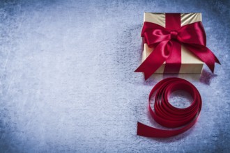 Present box with rolled red tape on metallic background copyspace