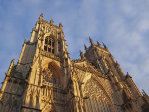 A front view of the towers at the entrance to york minster in sunlight against a blue cloudy sky