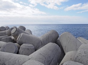 Concrete interlocking tetrapods used to prevent coastal erosion placed on a shoreline with a blue