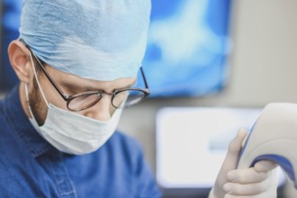 Doctor with mask looking down at medical equipment, focused ambiance