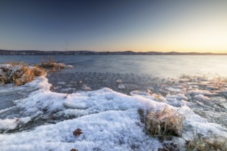 Snow-covered lakeshore with gentle waves at sunrise, Niederzell, Reichenau, Lake Constance,