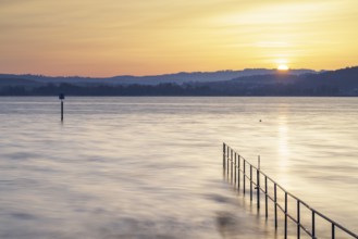 Sunrise over a calm lake with railings and distant hills, lido, Litzelstetten, Lake Constance,