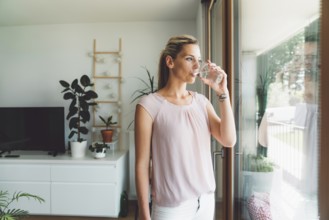 Smiling young caucasian woman taking her morning supplements, vitamin pills with a glass of water