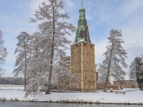 Historic castle tower on the lake in winter with snow-covered trees and a clear sky, Raesfeld,