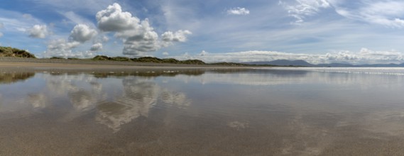 Peaceful panorama landscape of an empty golden sand beach with reflections of sky and sand dunes