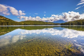 Clear water Pyramid Lake reflects the clouds and pine forests on shore. Frosty morning in the Rocky