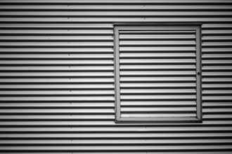 Close-up of the corrugated sheet metal façade of an industrial building with a metal window frame