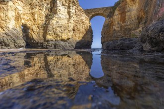 Yellow rocks and cliffs on a sandy beach. A bay by the sea, over which the old stone bridge of the