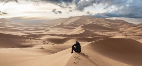 A person sitting in the Erg Chebbi desert in the African Sahara, Morocco, Africa