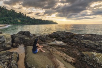 Tropical sea beach sunset with woman tourist on rock coast and ocean wave at Khao Lak, Phang Nga