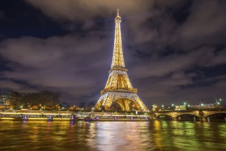 Paris, France, February 14, 2016: The Eiffel Tower golden lights, at night, reflected in the Seine