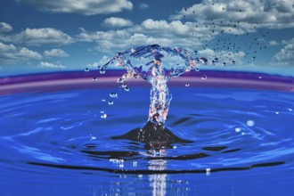 A splashing drop of water in front of a sky with white clouds and flying birds, highspeed