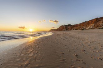 Beautiful sandy beach with red rocks and cliffs. Twilight at sunset with shallow waves on the