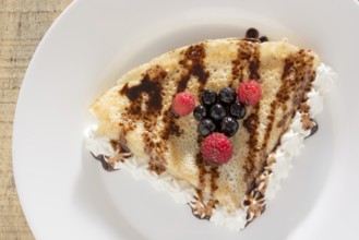 Fresh, golden pancakes with fruit and cream on a white plate with blurred background