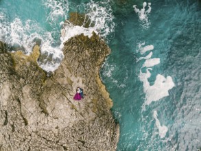 Man and woman lie embracing on the rocks by the blue foaming sea. View from above.