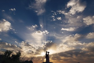 The bride and groom tenderly hug on the mountain in the rays of the setting sun.