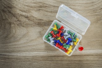Set of drawing pins in plastic box on wooden board
