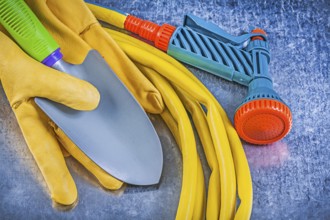 Set of rubber garden hose spray nozzle safety gloves spade on metallic background gardening concept