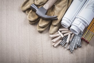 Wooden meter dowels blueprint rolls claw hammer leather protective gloves and metal nails on wood
