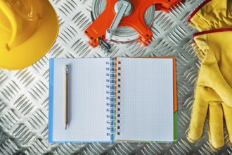 Safety gloves hard hat tape measure notebook pencil on corrugated metal sheet