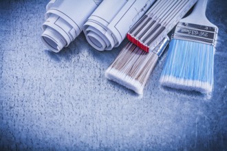 Paintbrushes wooden meter blueprints on metallic background close up view