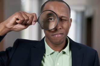 Handsome African American man looking through a large magnifying glass