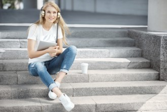 Happy young woman with vintage headphones and a cup of coffee to go, surfing the internet on a
