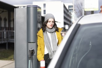 Woman in yellow jacket at e-charging station next to an electric car, environmentally friendly
