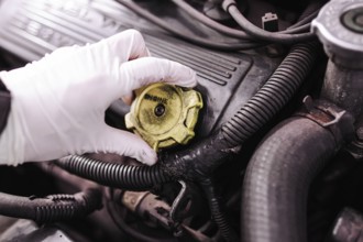 A gloved hand removing the cap from a car engine for maintenance