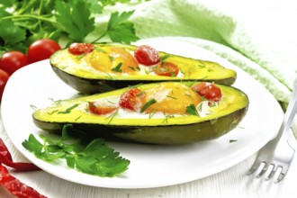 Scrambled eggs with cherry tomatoes in two halves of avocado in a plate, green towel and fork on