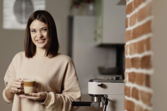 Woman with a cup of coffee beside an espresso machine and brick wall