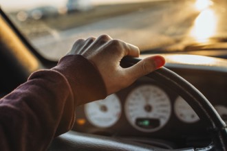 A hand on a steering wheel inside a car with a sunset view outside