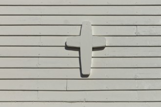Closeup of white painted wood cross on a white wooden wall