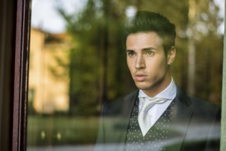 Handsome young man or bridegroom looking through the window
