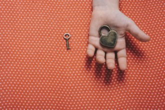 Hand holding a heart shaped lock and key on a red background