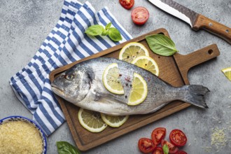 Raw fish dorado with ingredients lemon, fresh basil, cut cherry tomatoes, uncooked rice on wooden