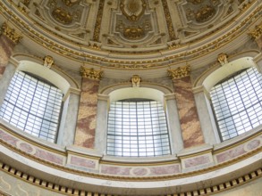 Detailed baroque ceiling with gilded decorations and large windows inside a historic building,