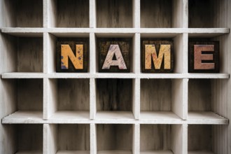 The word NAME written in vintage ink stained wooden letterpress type in a partitioned printer's