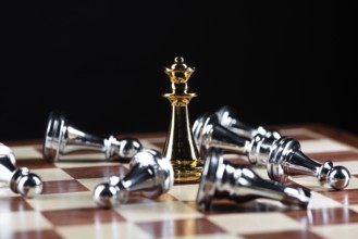 Gold queen chess defeats silver figures on wooden chessboard. Intellectual duel and tactical battle