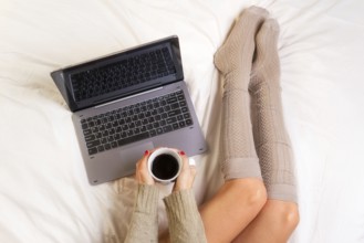 Soft photo of woman on the bed with laptop and cup of coffee in hands, top view point
