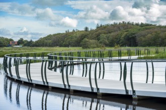 A modern bridge winds its way across the water against a backdrop of clouds and nature, Tureluur