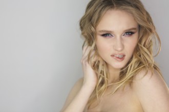 Portrait of the young beautiful woman with blonde curly hair on grey background