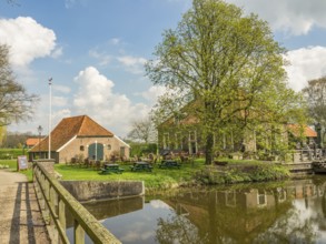 Rural scene with several buildings, a large tree and a small bridge crossing a river, Eibergen,