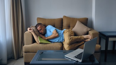 Young adult caucasian man felt asleep on a couch in front of laptoe. Tired man sleeps on sofa